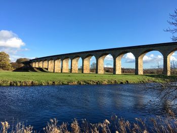 Arch bridge over river against clear blue sky