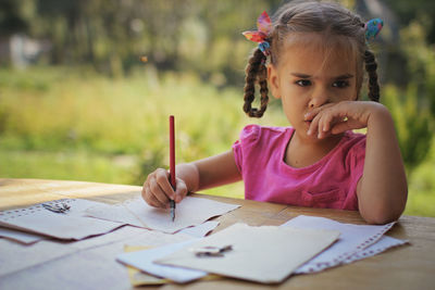 Cute girl looking away whole holding pencil outdoors