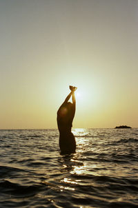 Rear view of woman in sea against clear sky during sunset