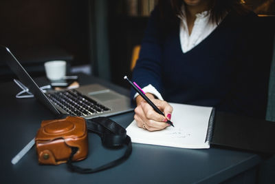 Midsection of businesswoman writing in diary at desk