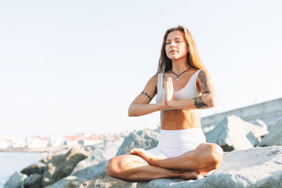 Young fit woman with long hair in white sport clothes practice yoga and meditation on sea beach