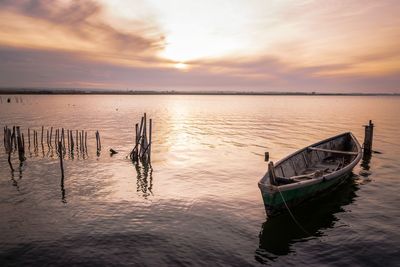 Boat moored in sea against sky during sunset