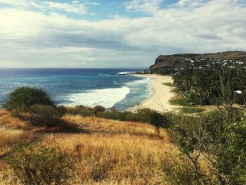 Scenic view of sea seen from grassy cliff against cloudy sky