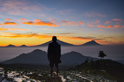 Rear view of man standing on mountain against sky during sunset