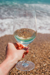 Woman hand with white wine glass on a turquoise mediterranean sea foam, waves and beach background