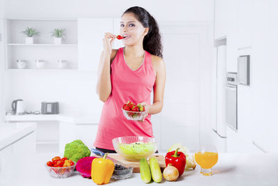 Portrait of woman eating strawberry while standing at home