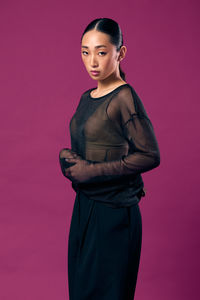 Portrait of young woman standing against yellow background