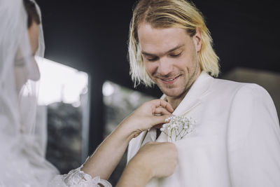 Bride adjusting boutonniere in smiling groom's pocket on wedding day