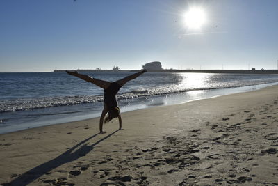 Rear view of woman practicing handstand at beach against sky