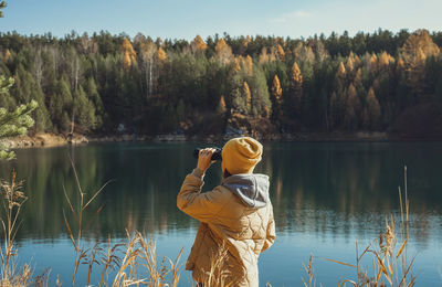 Young woman ecologist looking through binoculars at birds on lake against autumn forest birdwatching