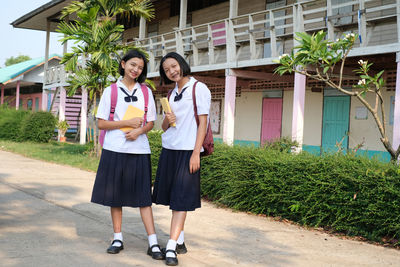 Portrait of friends in school uniforms while standing on road