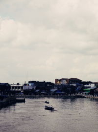 Sailboats in sea by buildings against sky