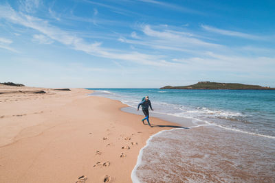 Rear view of woman walking at beach against sky