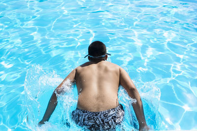Rear view of shirtless man swimming in pool