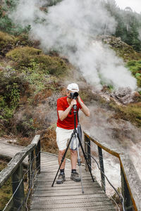 Man photographing with camera while standing on boardwalk against mountain