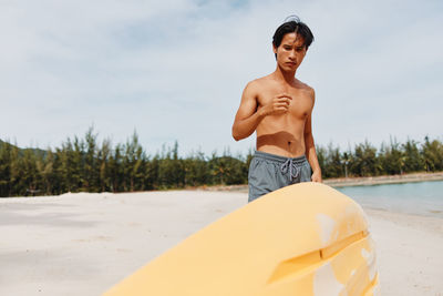 Portrait of shirtless man sitting on beach against sky