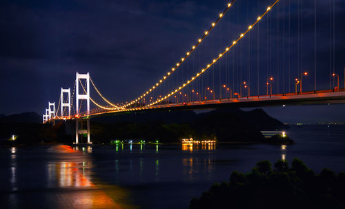 Illuminated bridge over river against sky at night