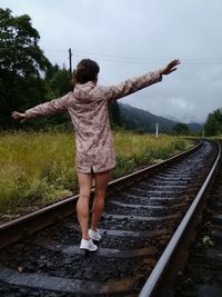 Rear view of woman walking on railroad tracks against sky