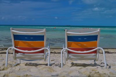 Deck chairs on beach against sky