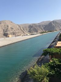 Scenic view of river by mountains against clear blue sky