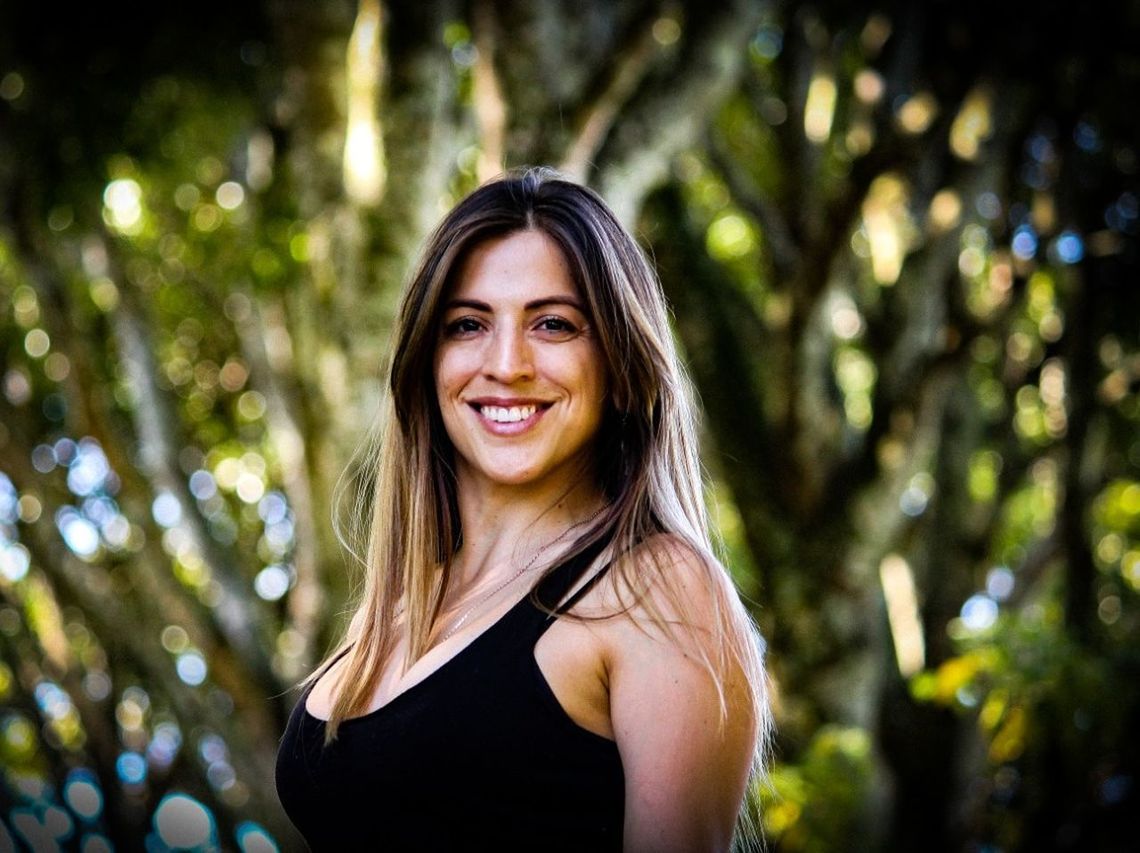 PORTRAIT OF SMILING YOUNG WOMAN STANDING AGAINST TREES IN FOREST