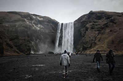 People standing by waterfall against mountain