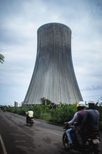 Rear view of man riding bicycle on road in city against sky