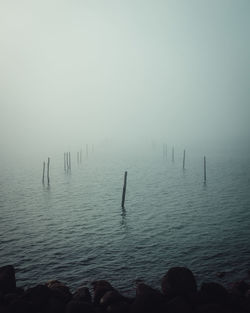 Silhouette wooden posts in sea against sky