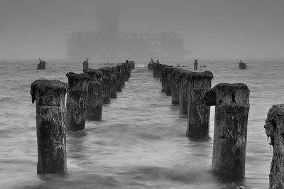 Wooden posts in sea against sky