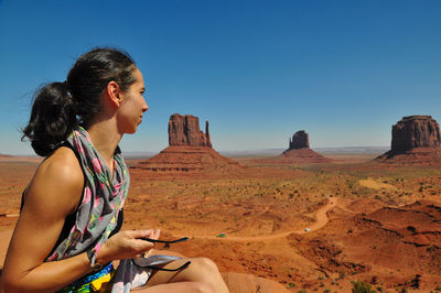 Woman looking at rock formations against clear blue sky