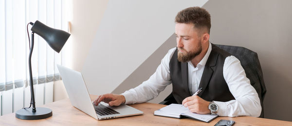 Business planning. thoughtful bearded man using laptop and writing in notebook