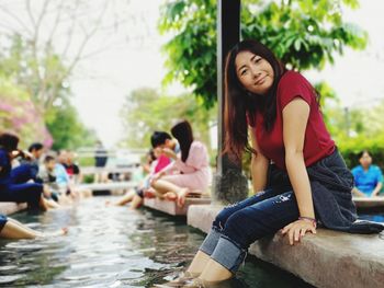 Portrait of woman sitting while dipping legs in pond