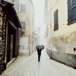 Rear view of man walking on footpath amidst buildings