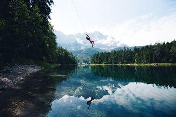 WOMAN PARAGLIDING OVER LAKE AGAINST TREES