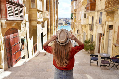 Back view of tourist girl holding hat descends stairs in the old town of valletta, unesco, malta.