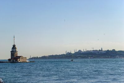 Sailboats in sea by buildings against sky