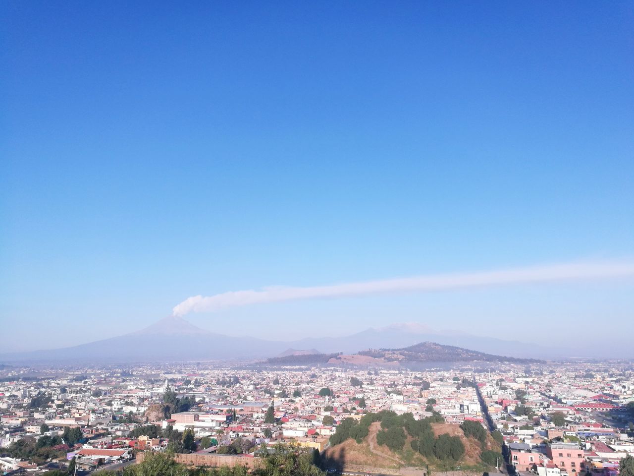 sky, building exterior, architecture, built structure, blue, city, copy space, cityscape, building, mountain, nature, residential district, no people, environment, day, outdoors, high angle view, clear sky, townscape, settlement