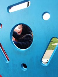 Happy toddler boy seen from blue play equipment at playground