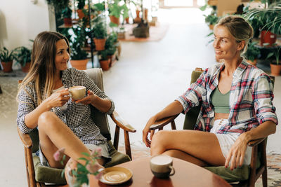 Two young attractive women have fun chatting and drinking coffee while sitting in a cafe.