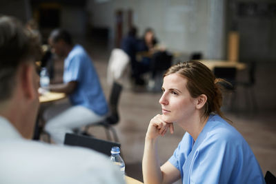 Confident female nurse looking at mature doctor while sitting in hospital cafeteria