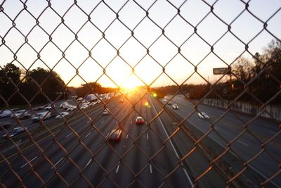 Road seen through chainlink fence against sky during sunset