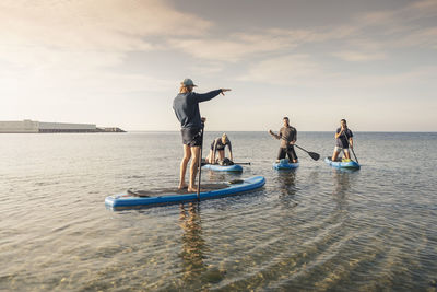 Man and women learning to row paddleboard from male instructor in sea