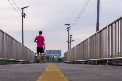 Rear view of man walking on bridge against sky