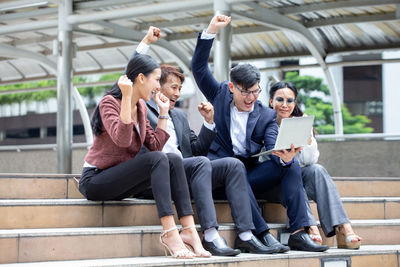 Full length of friends sitting on mobile phone