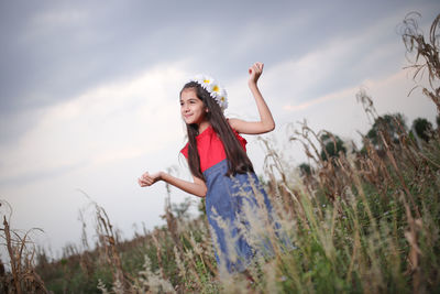 Smiling cute girl standing amidst plants on field during sunset