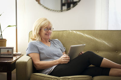 Happy woman using tablet computer while sitting on sofa at home