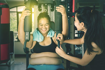 Happy young woman exercising with trainer at gym