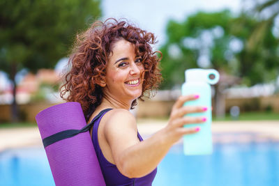 Horizontal view of curly hair woman dressed in a yoga outfit holding a bottle of water. 