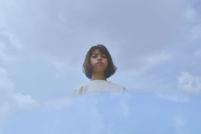 Low angle portrait of young woman standing against sky