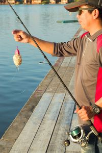 Man fishing while standing on pier over sea